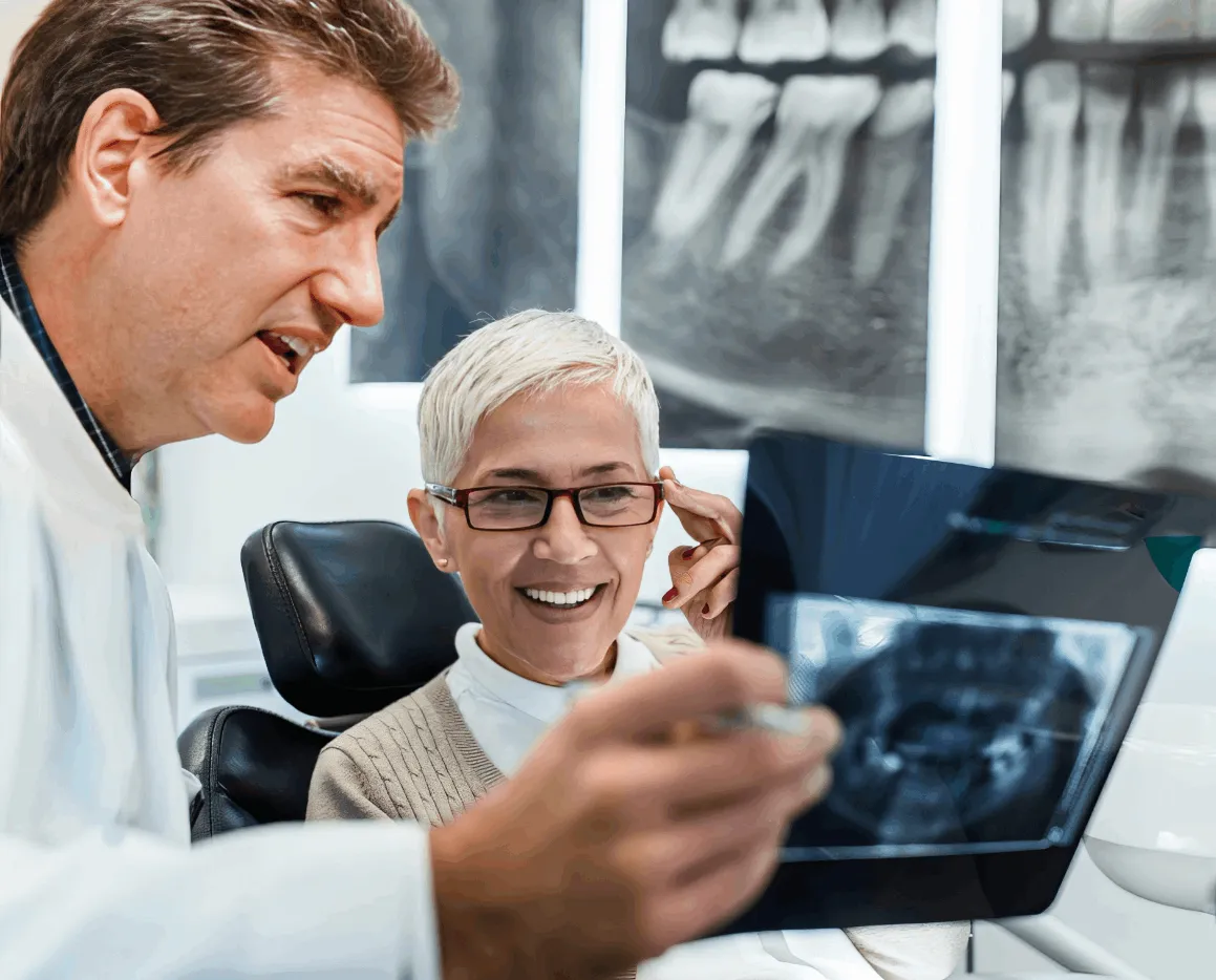 Dentist showing a dental X-ray to a smiling female patient wearing glasses in a dental office.
