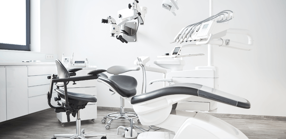 Modern dental clinic with black dental chair, dentist stool, and dental equipment in a bright room.
